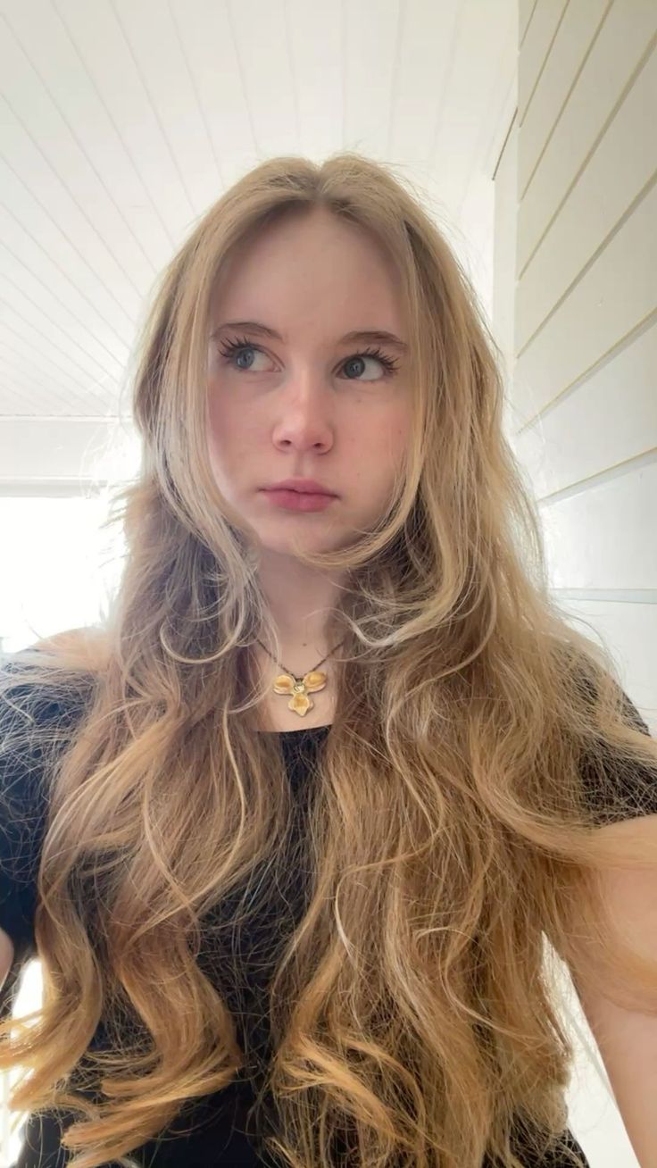 Young woman with long blonde hair wearing a black shirt and necklace indoors