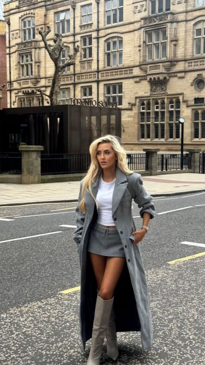Woman with long blonde hair in a gray coat and mini skirt on a city street