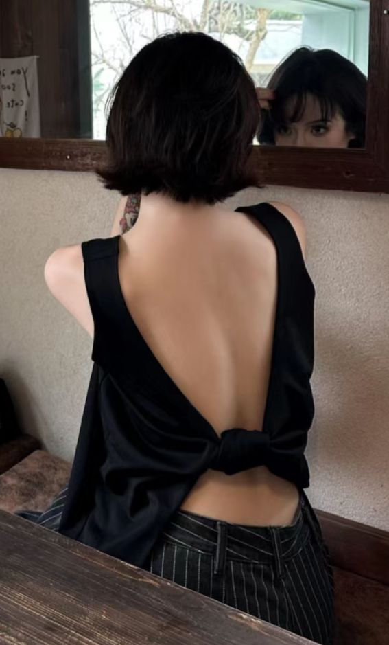 Woman with short black hair in an open-back top and striped pants, looking in a mirror
