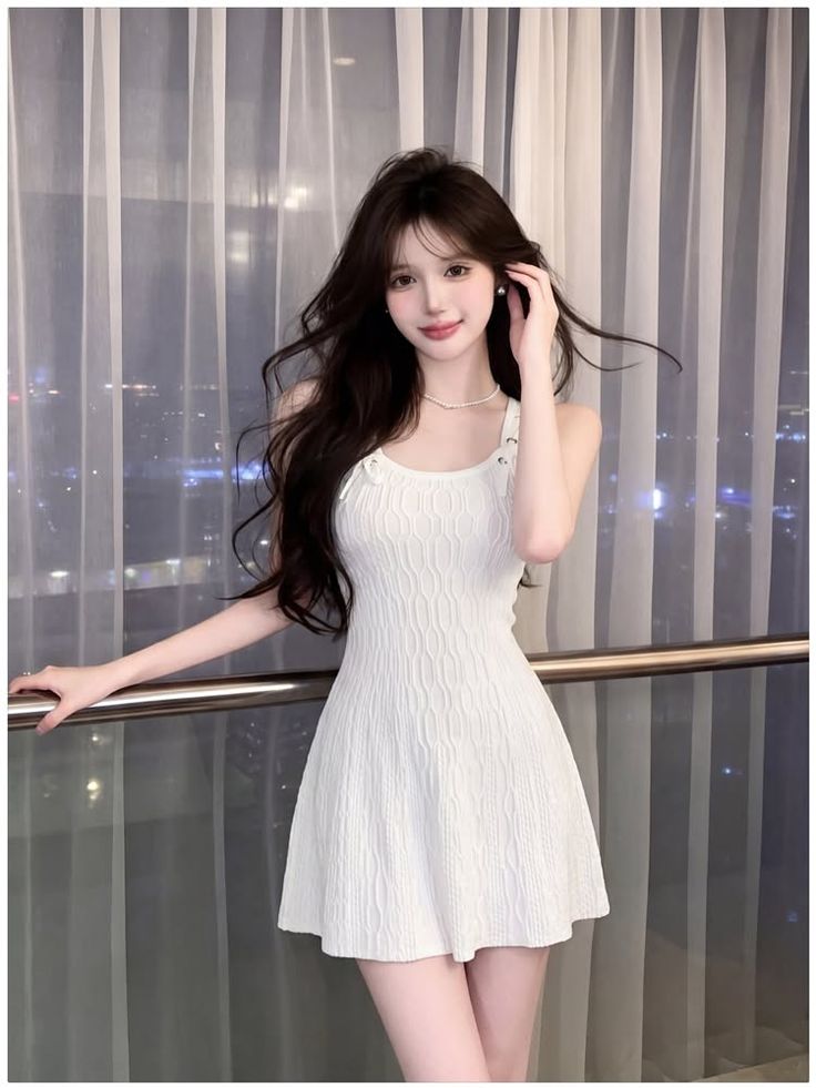 Woman in a white dress and pearl necklace indoors at night with a cityscape view
