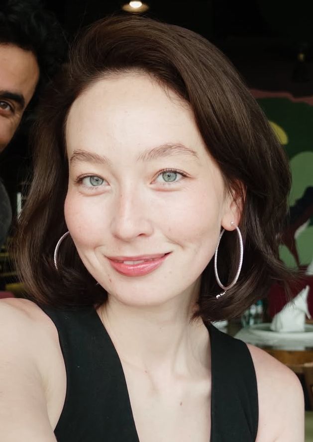 Woman with short brown hair and blue eyes smiling, wearing hoop earrings