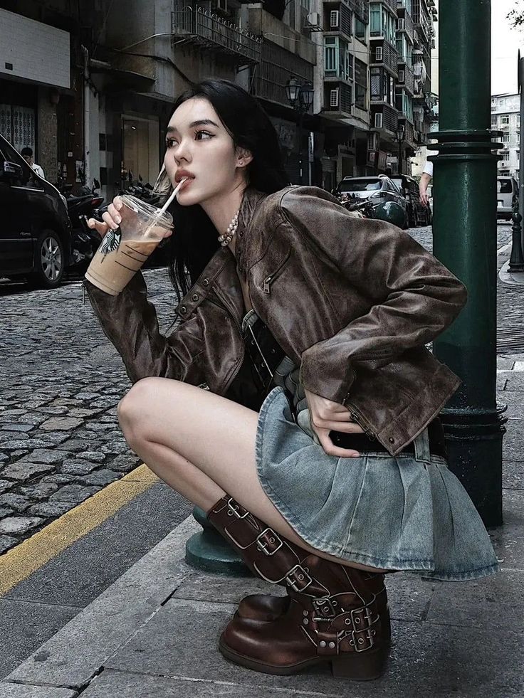 Woman in a leather jacket and denim skirt crouching on a cobblestone street
