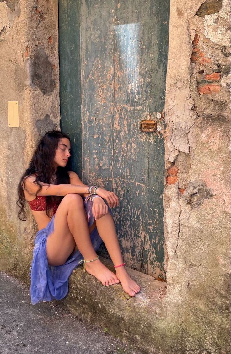 Woman with long dark hair sitting barefoot against an old wooden door