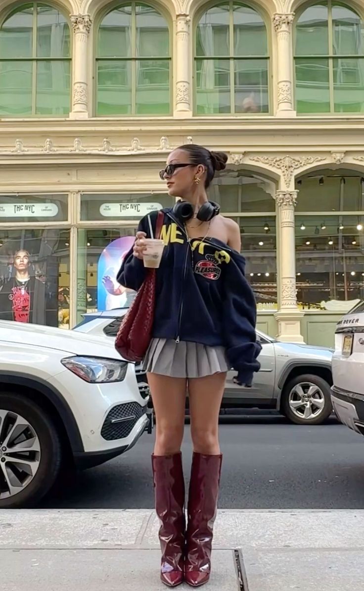 Woman in a pleated skirt and hoodie with high boots on a city street