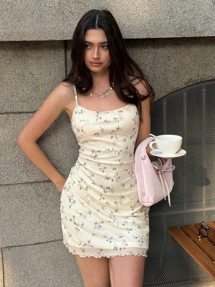 Woman in a floral dress holding a pink bag and a teacup outdoors