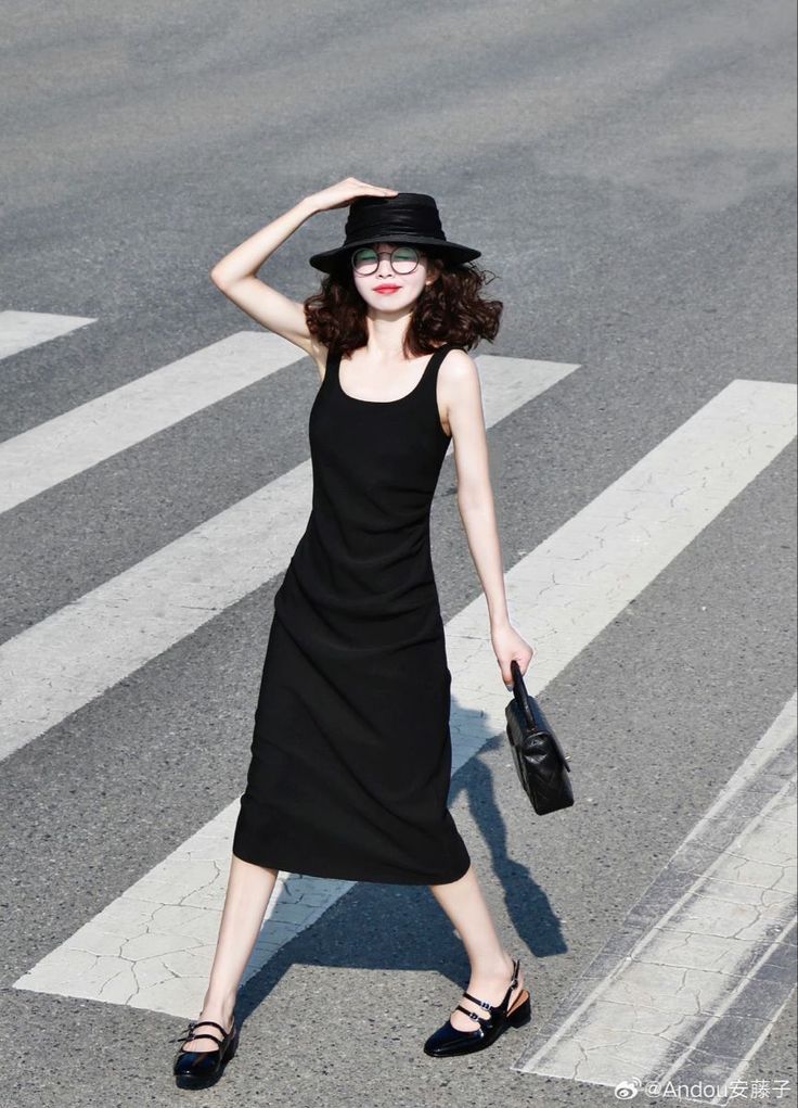 Woman in a black dress, hat, and glasses walking on a crosswalk