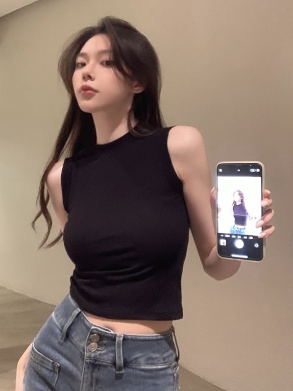 Woman in a black top and blue jeans holding a phone showing a photo of herself