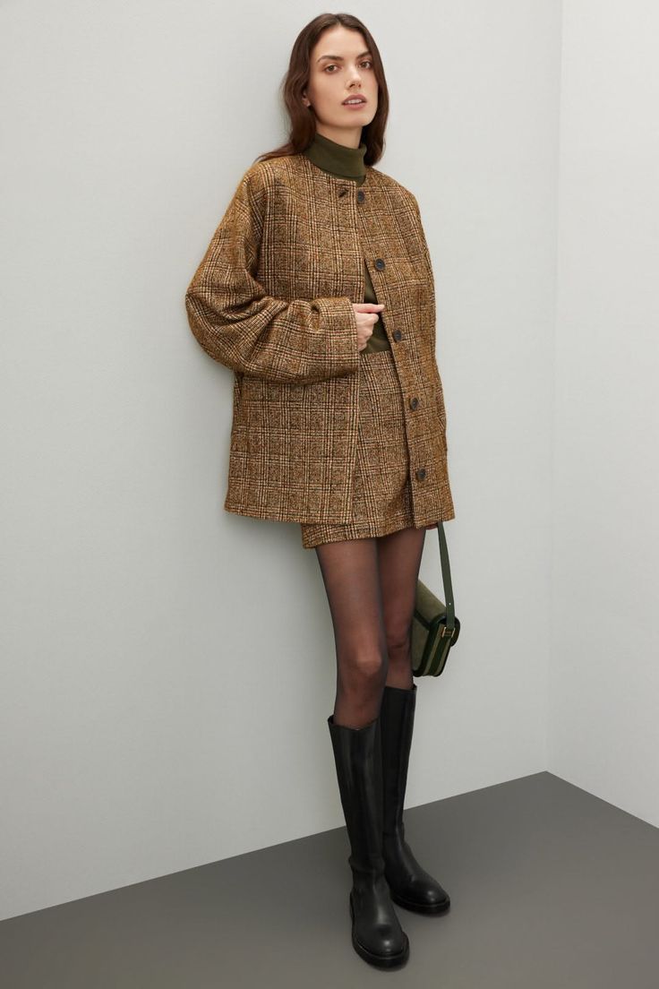 Woman in a plaid jacket and mini skirt with black boots and a green bag