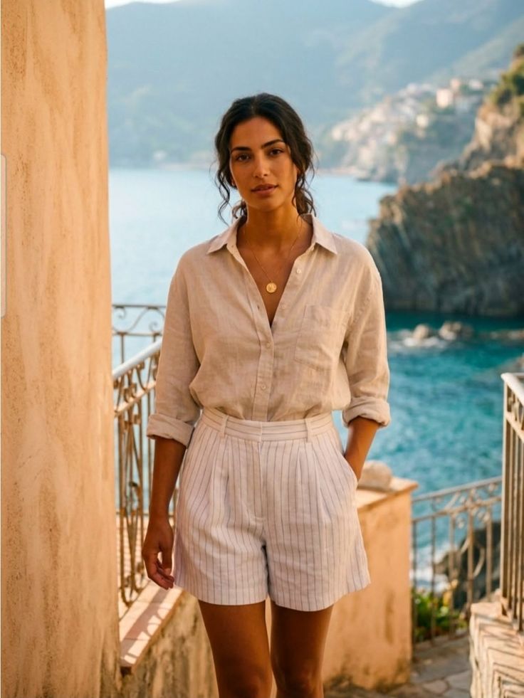 Woman in a linen shirt and striped shorts on a coastal balcony