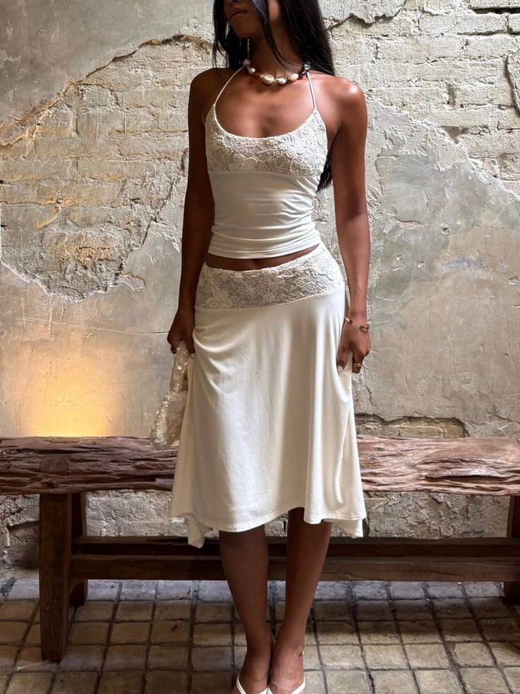 Woman in a white lace-trimmed dress and pearl necklace standing indoors