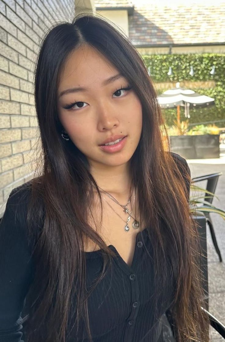 Young woman with long dark hair wearing a black top and layered necklaces outdoors