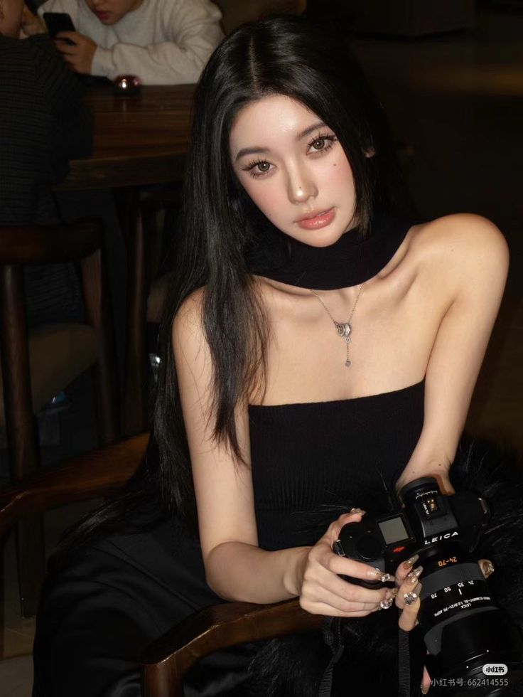 Woman with long black hair wearing a strapless top and choker, holding a camera