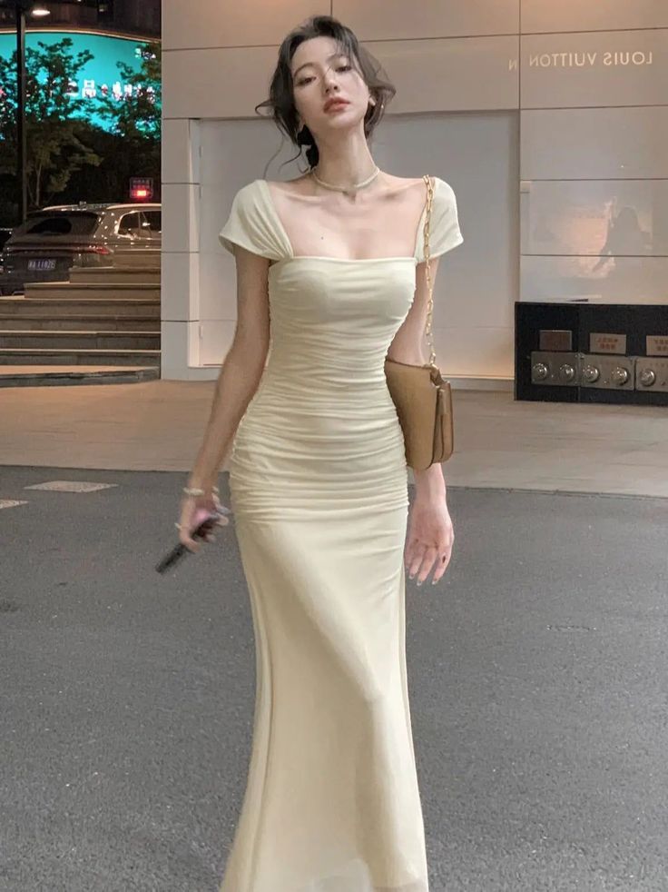 Woman in a long ruched dress and shoulder bag on a city street at night