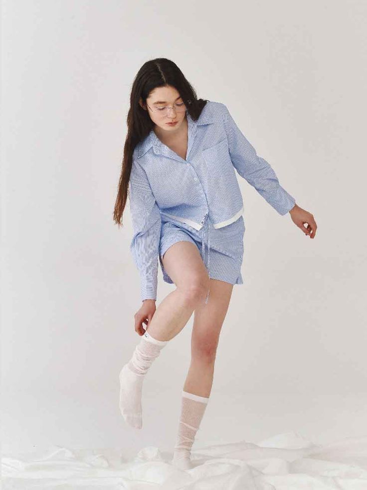 Woman in blue striped pajamas and glasses adjusting her sock indoors