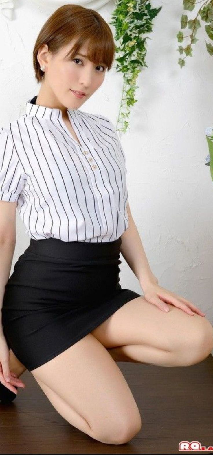 Woman with short hair in a striped shirt and black skirt kneeling indoors