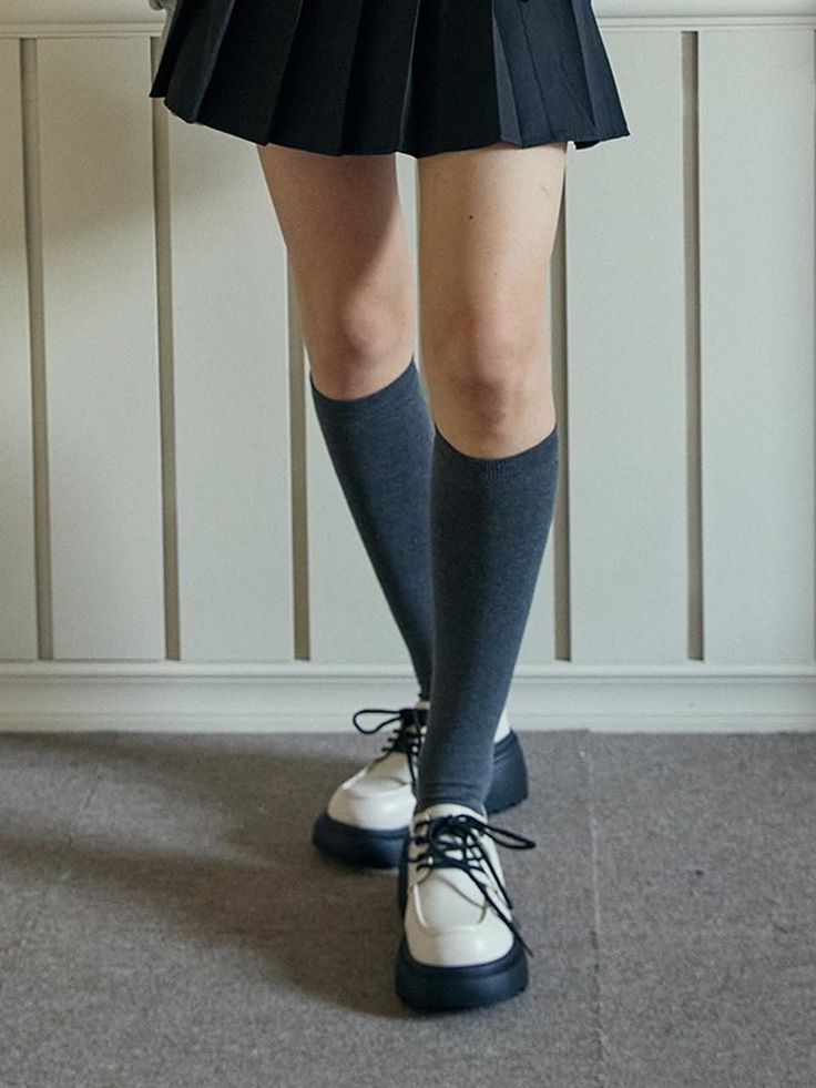 Person wearing a pleated skirt, knee-high socks, and chunky shoes indoors