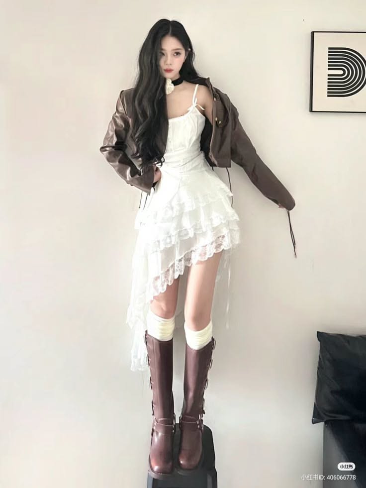 Woman with long dark hair wearing a white dress and brown jacket indoors