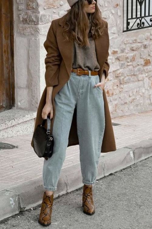 Woman in a brown coat, light wash jeans, and ankle boots on a street