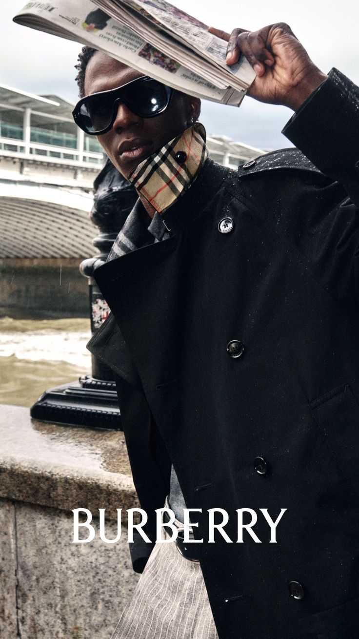 Person in a black coat and sunglasses holding a newspaper over their head in the rain