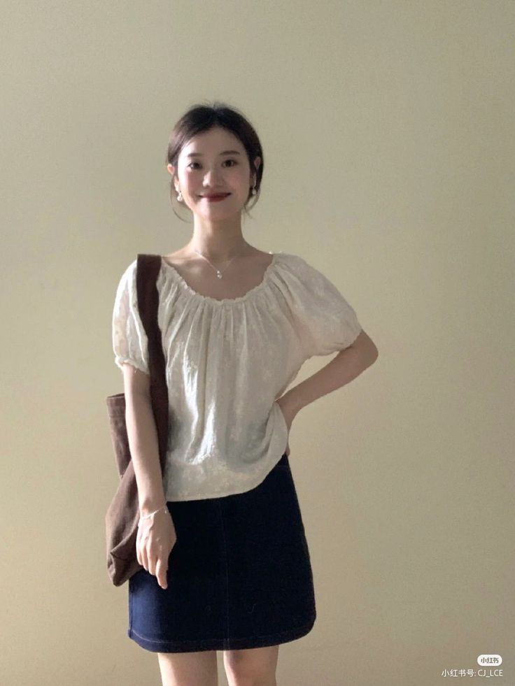 Woman in a white blouse and dark skirt with a shoulder bag indoors