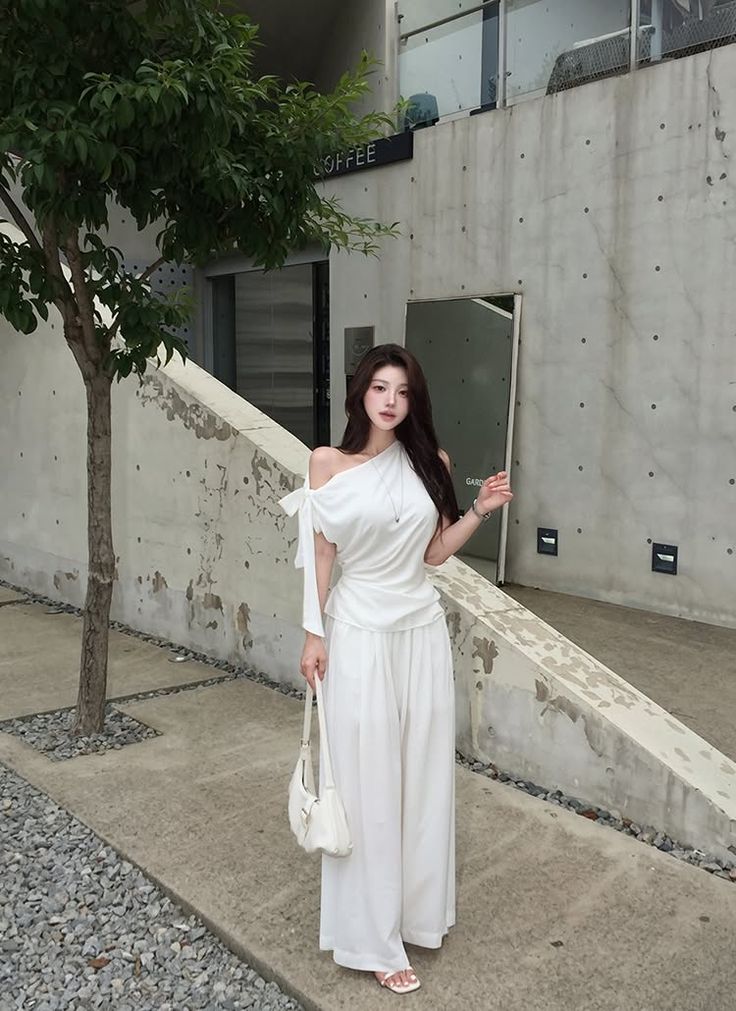 Woman in a white off-shoulder top and wide-leg pants standing outdoors