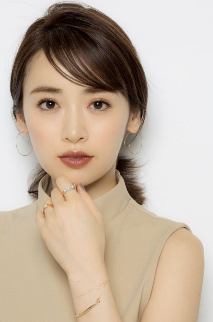Woman with brown hair wearing a sleeveless top and jewelry against a white background
