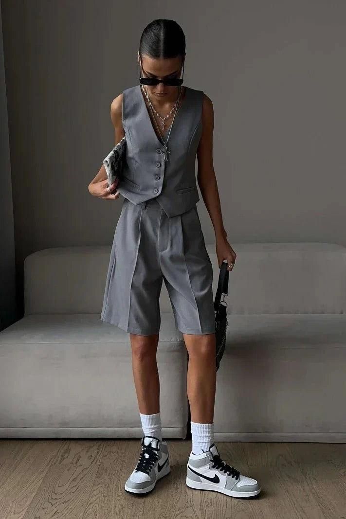 Person in a gray vest and shorts with sunglasses and sneakers indoors
