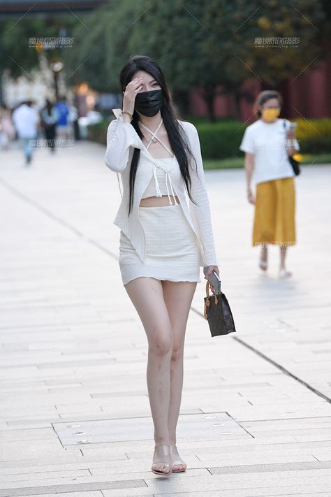 Woman in a white crop top and mini skirt with a black mask walking outdoors