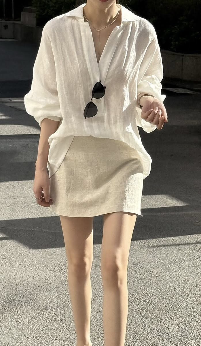 Person in a white shirt and mini skirt with sunglasses hanging from the collar