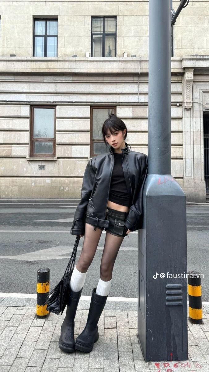 Woman in a black leather jacket and shorts leaning on a lamppost