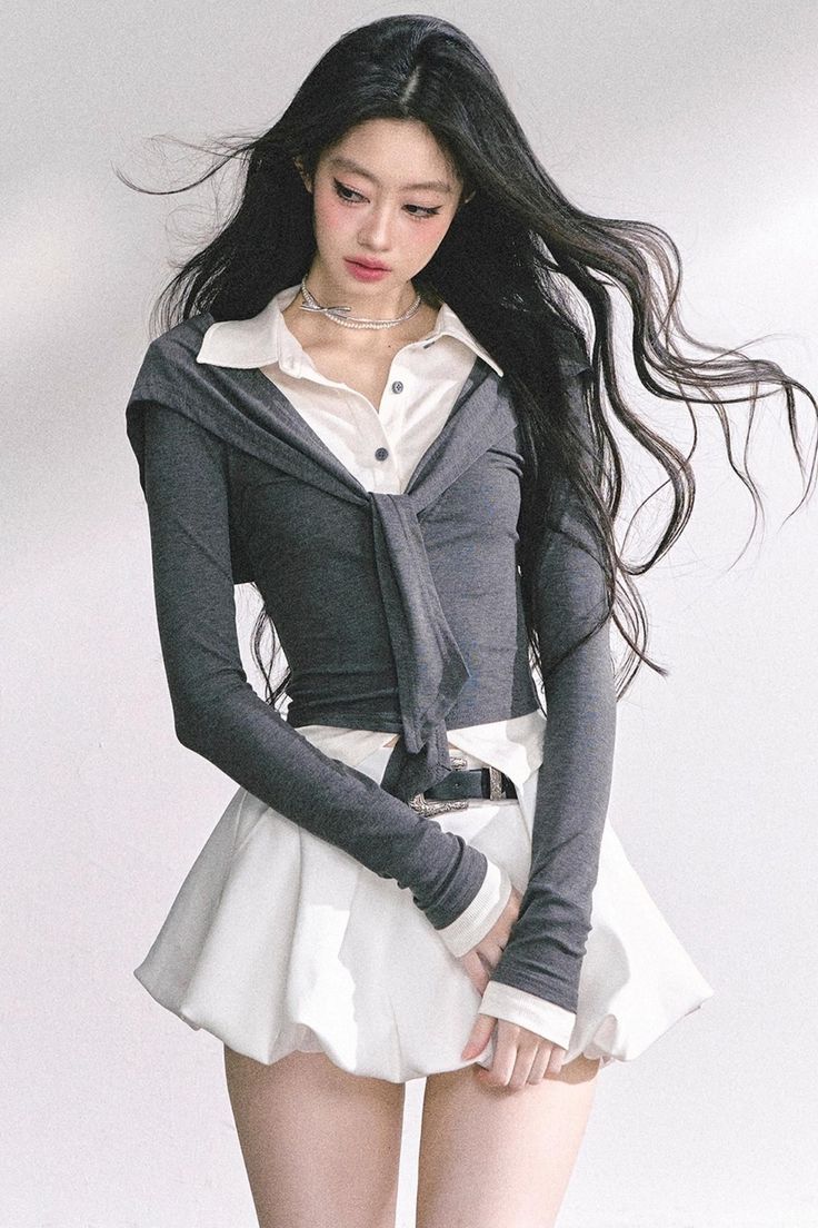 Woman with long black hair wearing a white shirt and gray cardigan over a white skirt