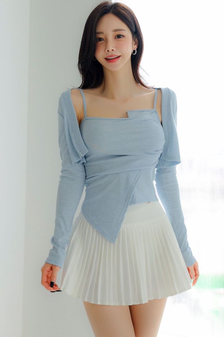 Woman with long dark hair wearing a light blue top and white pleated skirt indoors