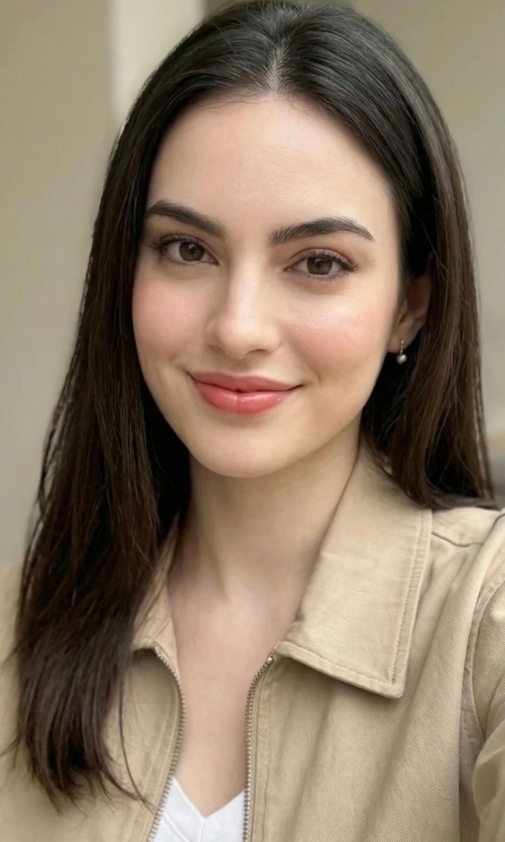 Woman with long dark hair and a tan jacket smiling at the camera