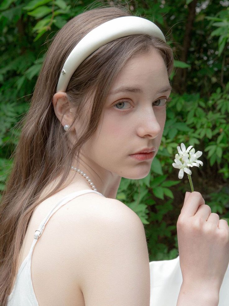 Woman with long hair and a white headband holding a white flower outdoors