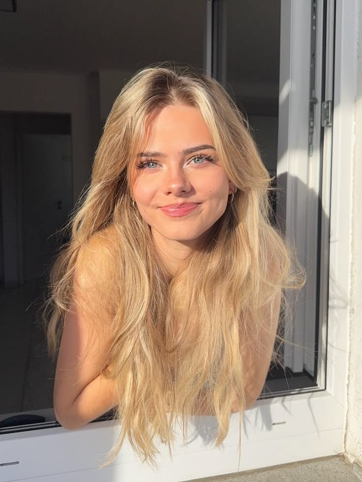 Young woman with blonde hair looking out a window in golden hour light