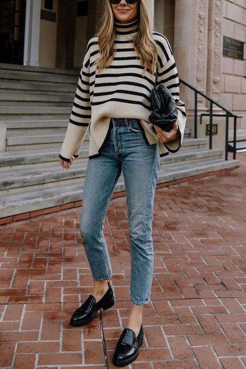 Woman in a striped sweater, blue jeans, and black loafers on a brick pavement