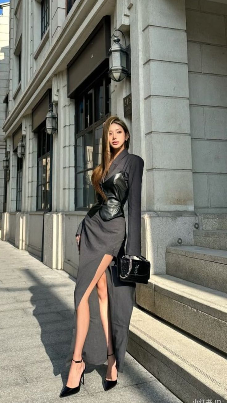 Woman in a black leather top and slit dress posing on a city street
