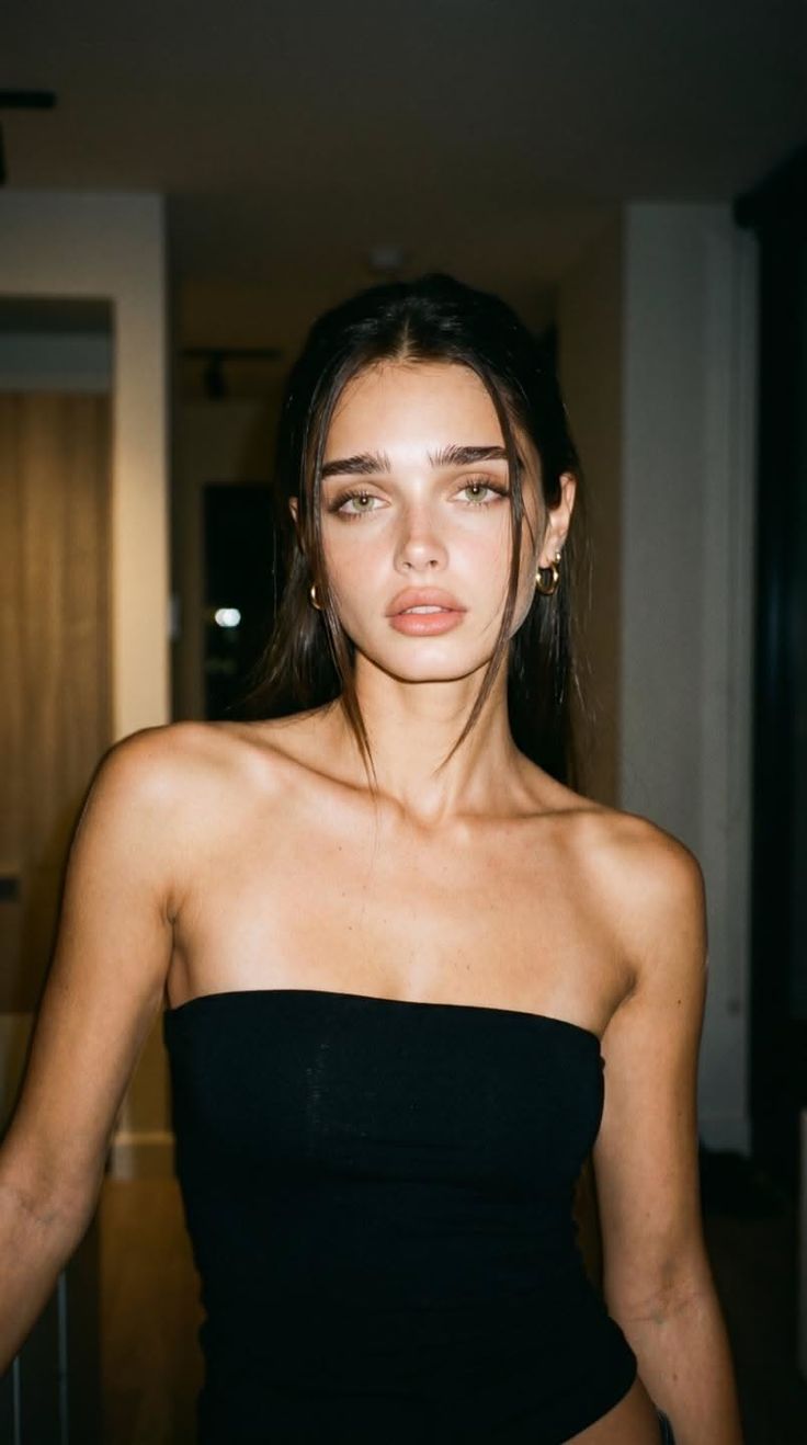 Woman with dark hair and green eyes wearing a black tube top indoors