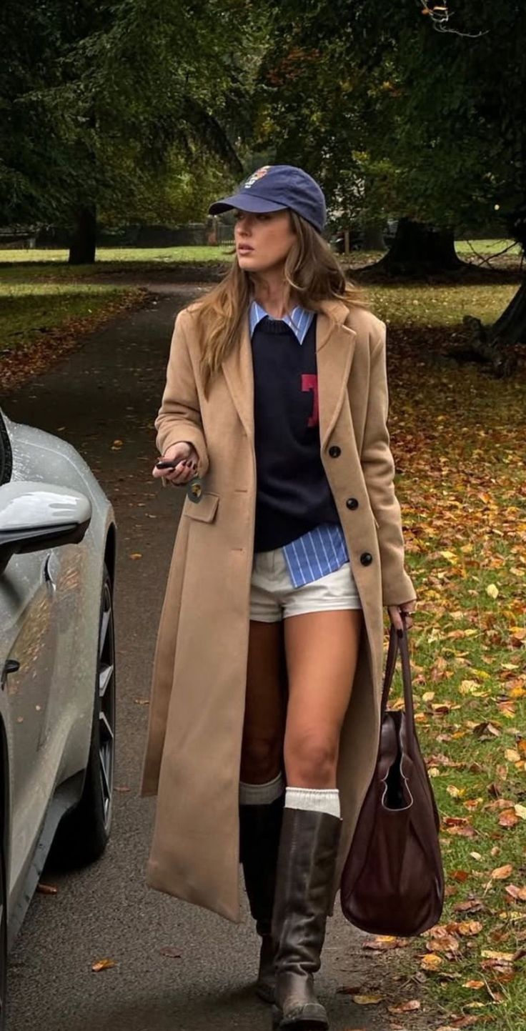 Woman in a long coat, shorts, and boots walking outdoors with autumn leaves