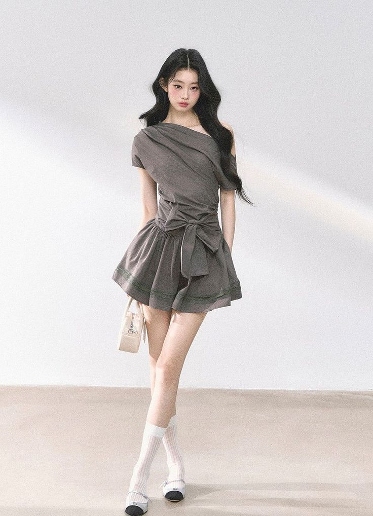 Woman with long black hair wearing a gray one-shoulder dress and white socks