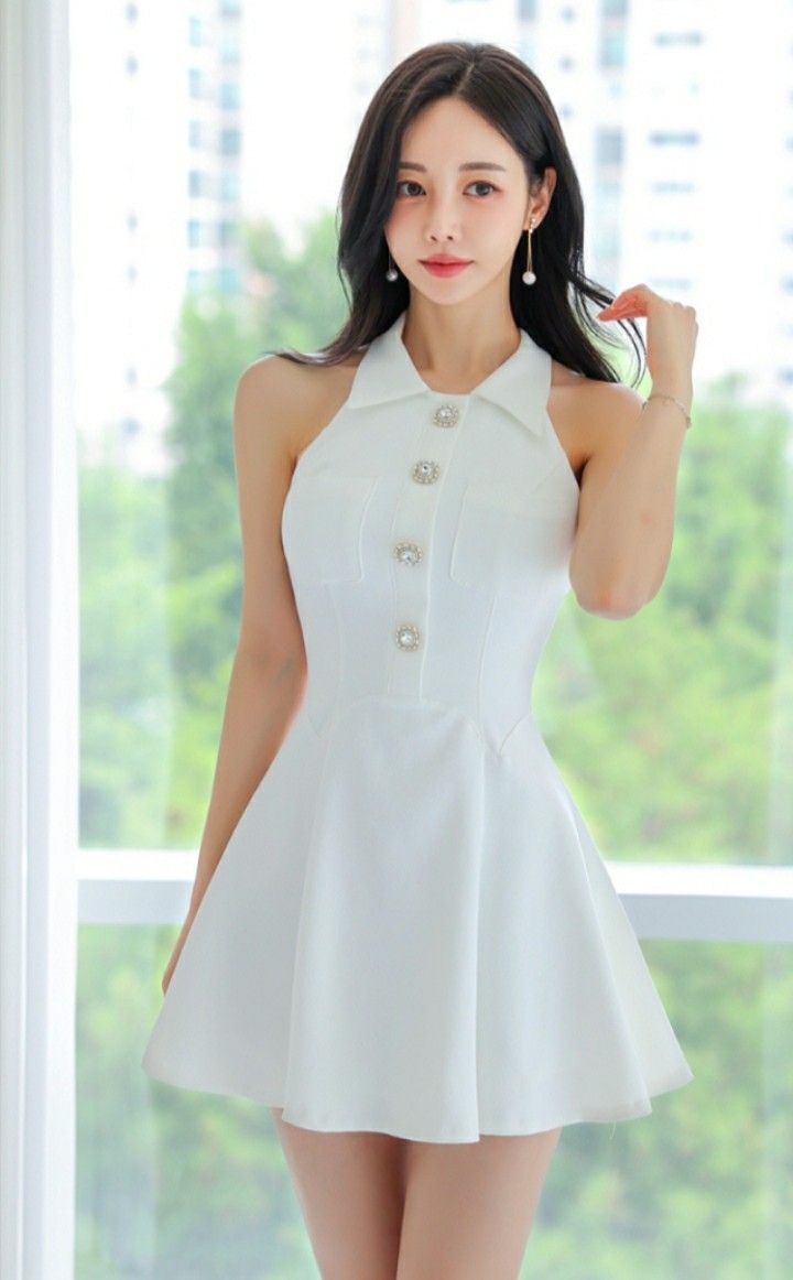 Woman in a white halter dress with pearl earrings standing indoors