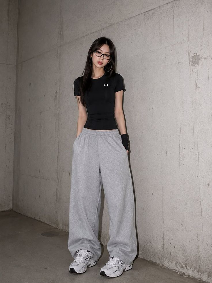 Woman with long hair and glasses wearing a black t-shirt and sweatpants indoors