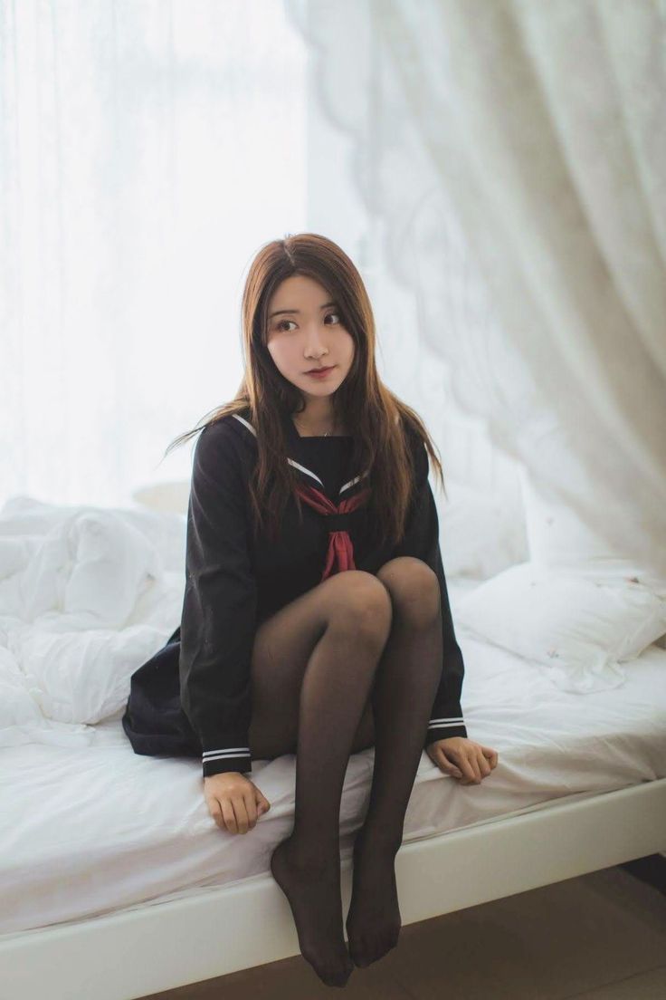 Woman in a school uniform and black pantyhose sitting on a bed