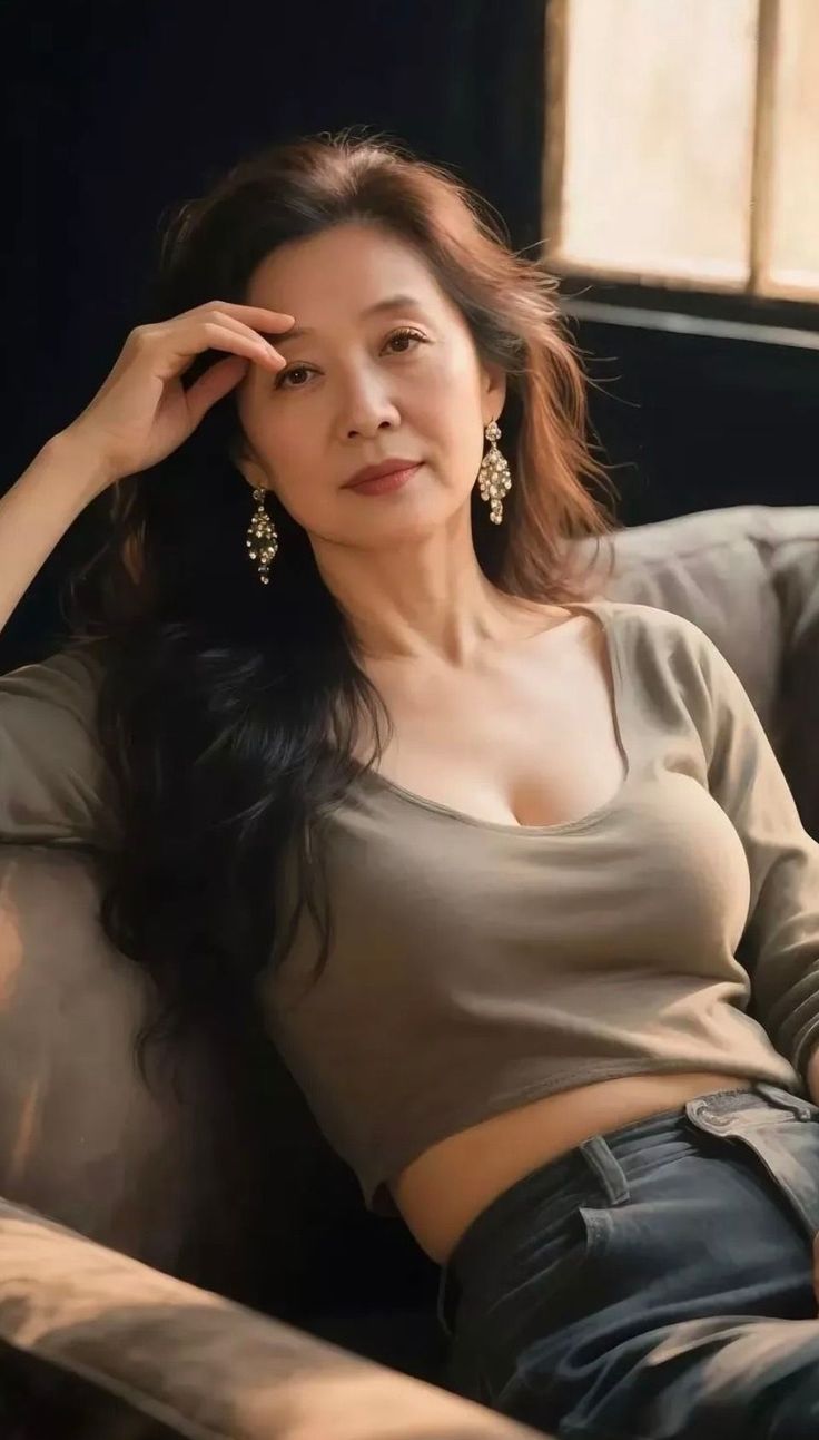 Woman with long hair and large earrings wearing a crop top, sitting indoors