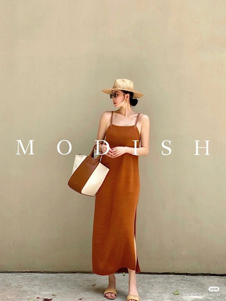 Woman in a brown maxi dress, straw hat, and sunglasses holding a tote bag