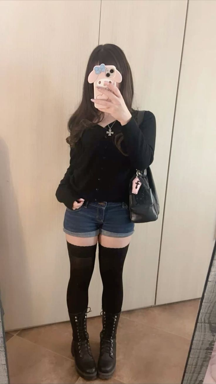Person in denim shorts, thigh-high socks, and combat boots holding a phone