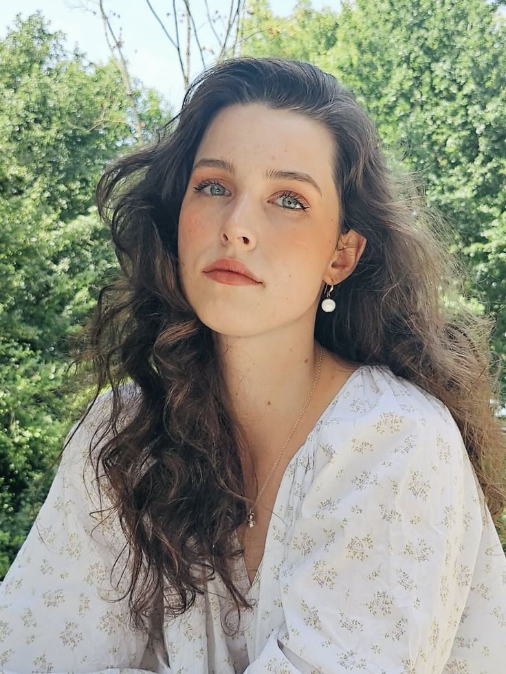 Woman with long wavy hair wearing a white floral blouse outdoors