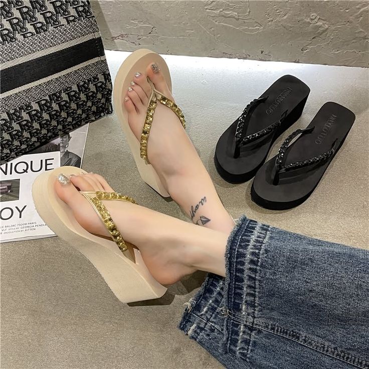Person wearing wedge sandals and jeans, with another pair of sandals nearby