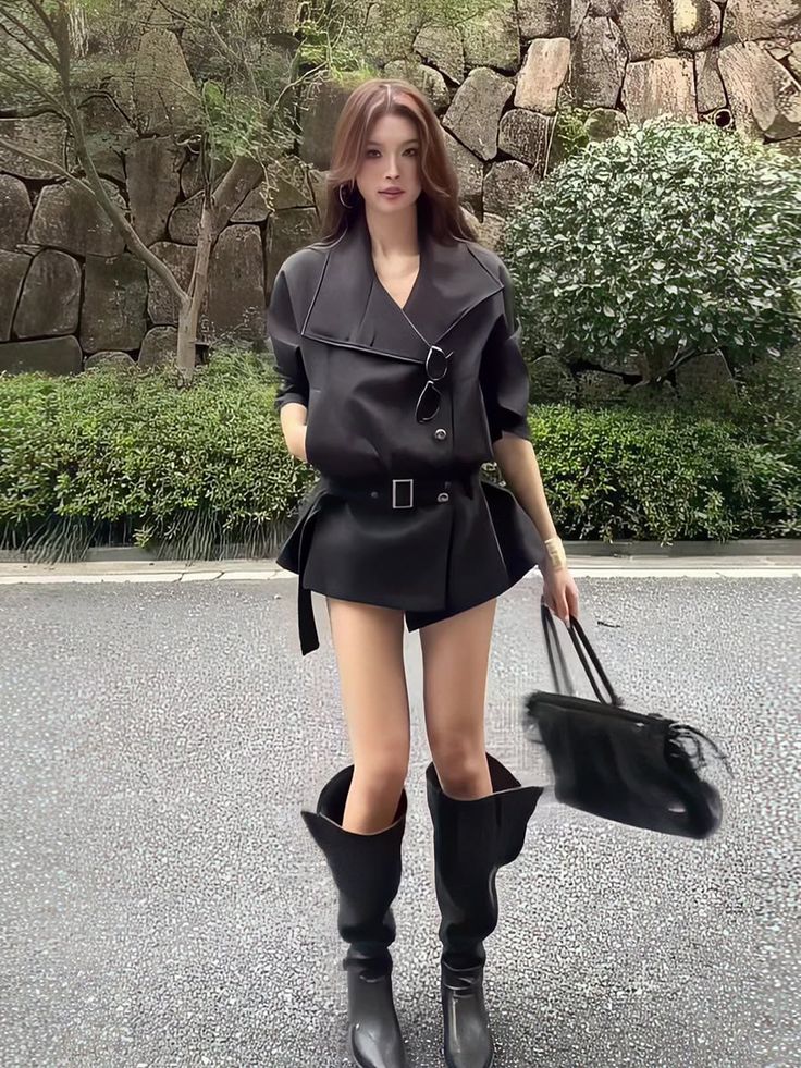 Woman in a black outfit and knee-high boots standing outdoors