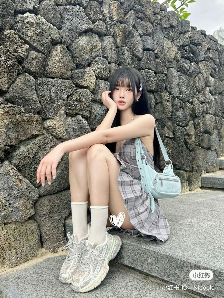 Woman with long black hair and bangs wearing a plaid dress and sneakers, sitting outdoors